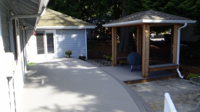 Design Build, Deck replacment in Bellingham. Low maintenance Azek decking with a gental curve and a covered BBQ area on the lower level. The pavers below carry the curved element as well.